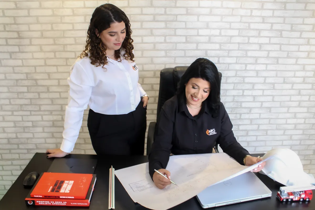 Equipe da Samartino Engenharia revisando projeto de sistema de sprinklers, com capacete e materiais técnicos sobre a mesa